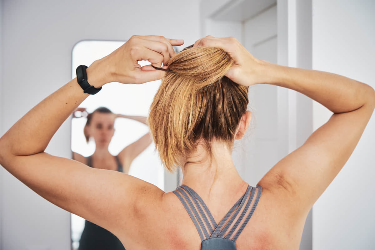 Woman in a sports bra tying her hair while looking in the mirror.