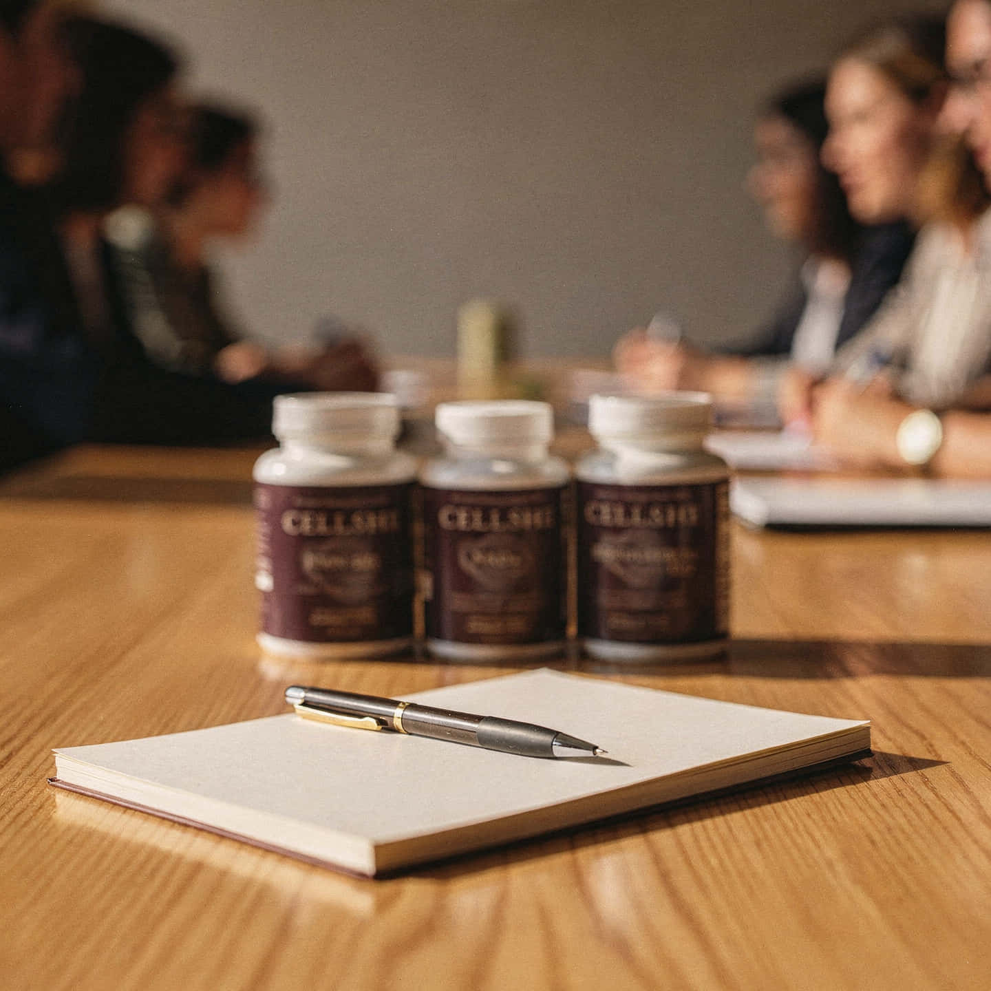 Three CELLSHE supplement bottles on a wooden table beside a notebook and pen