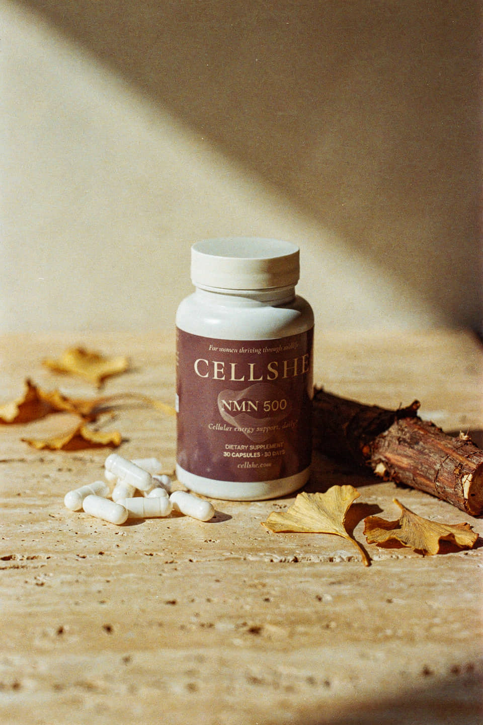 CELLSHE NMN 500 supplement bottle with capsules on a warm textured surface