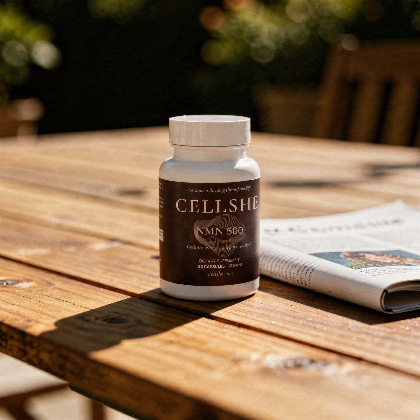 CELLSHE NMN 500 bottle on an outdoor wooden table beside a newspaper