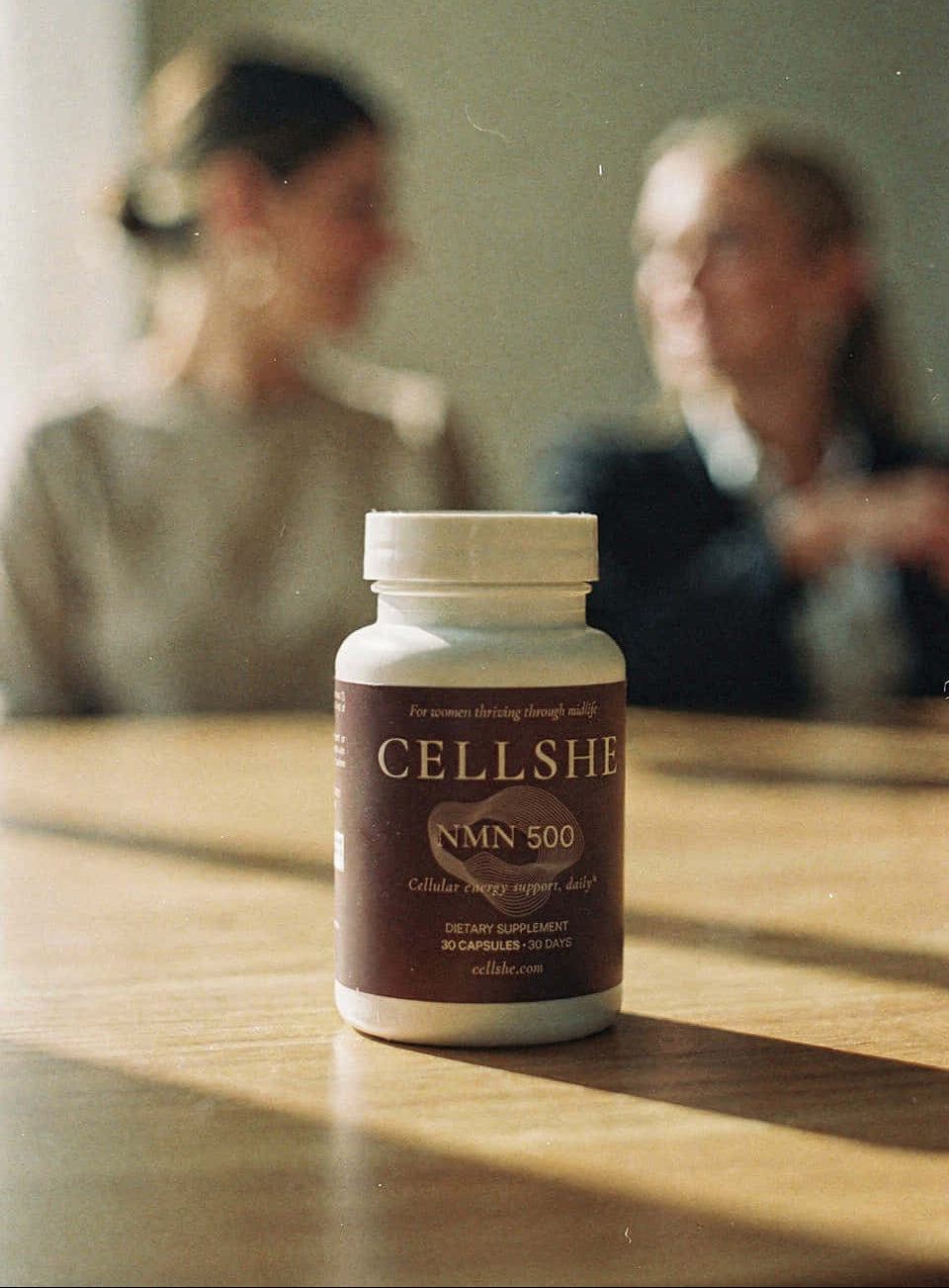 CELLSHE NMN 500 bottle on a table with two people in the background