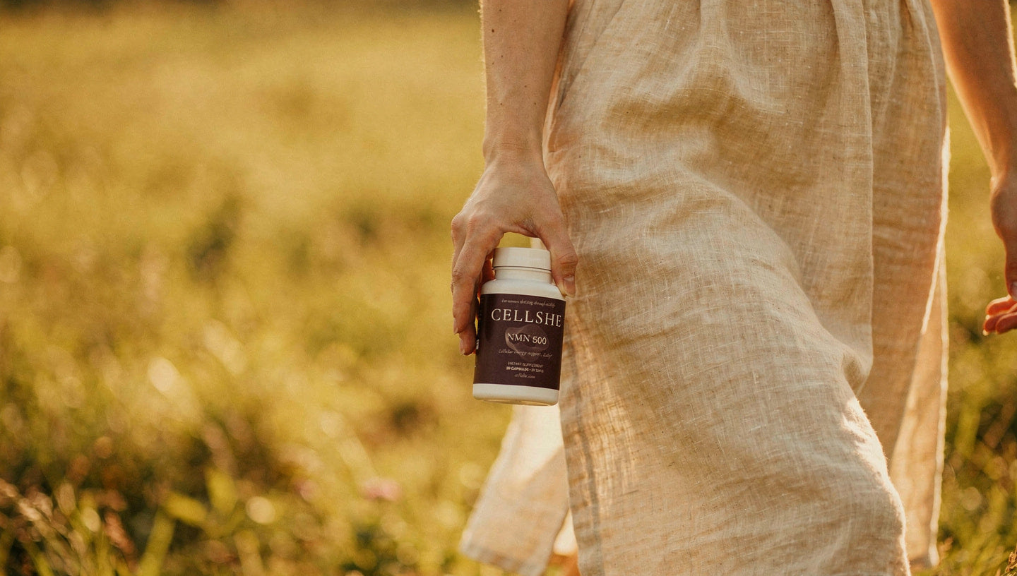 Woman holding a CELLSHE NMN 500 supplement bottle in a sunlit field